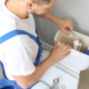 Plumber repairing toilet tank in restroom